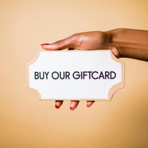 Close-up of a hand holding a 'Buy Our Giftcard' sign on a brown backdrop.
